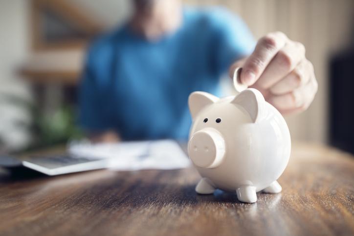 Someone in blue puts a coin inside a white piggy bank