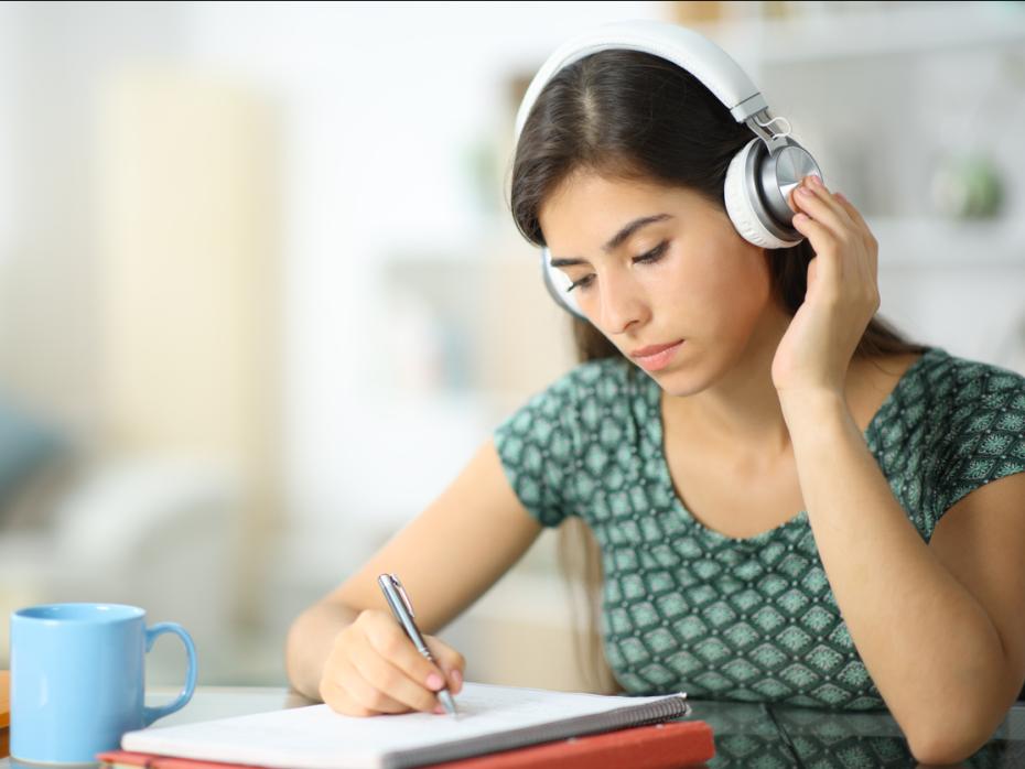 Female autistic student with noise-cancelling earphones writing in a notepad