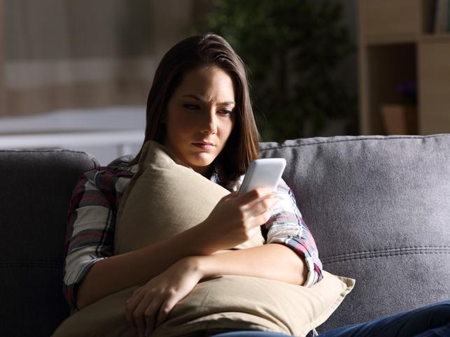 Young woman on couch with pillow looking at phone