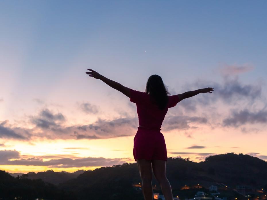 Silhouette of a woman standing in a field with her arms outstretched