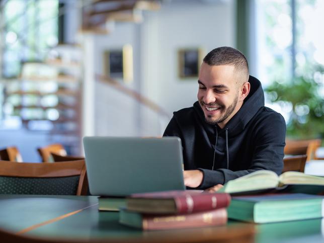 A student sits at a laptop in a library