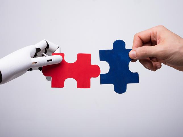 A robot and human hand put two jigsaw puzzle pieces together