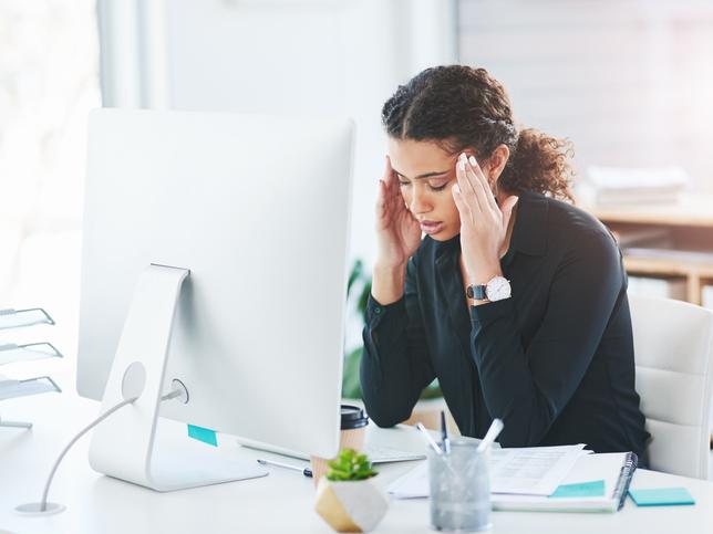 A woman massages her temples in front of a desktop computer