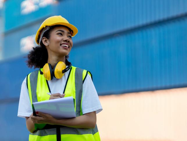 A woman in a hard hat writes on a clipboard