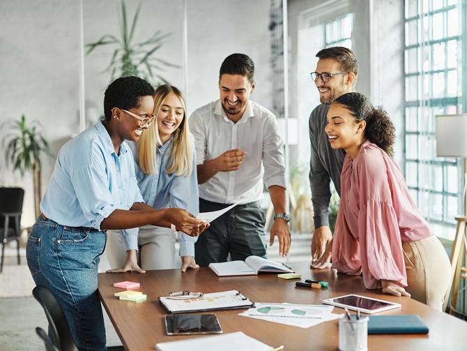 A group of people laugh over a sheet of paper in a well-lit office