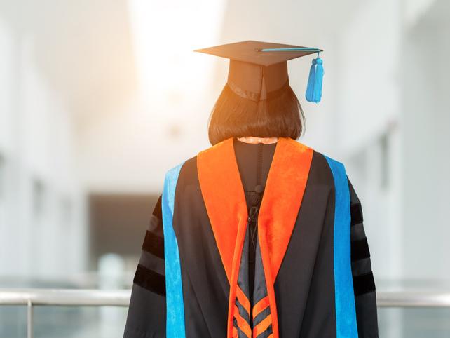 A PhD graduate in cap and gown stands with her back to the camera