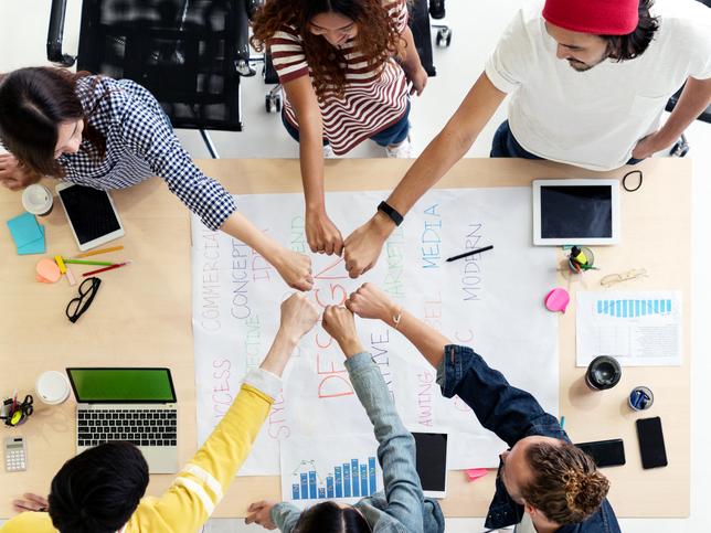 A group of students fist-bump over a table of work