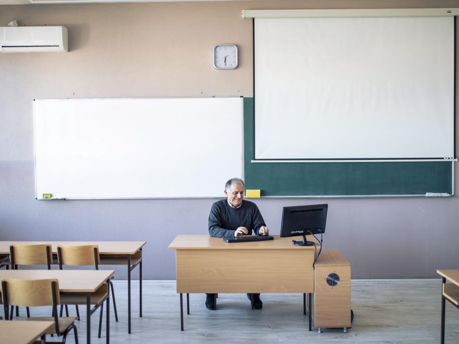 Teacher sitting at his desk in an empty classroom waiting for his students