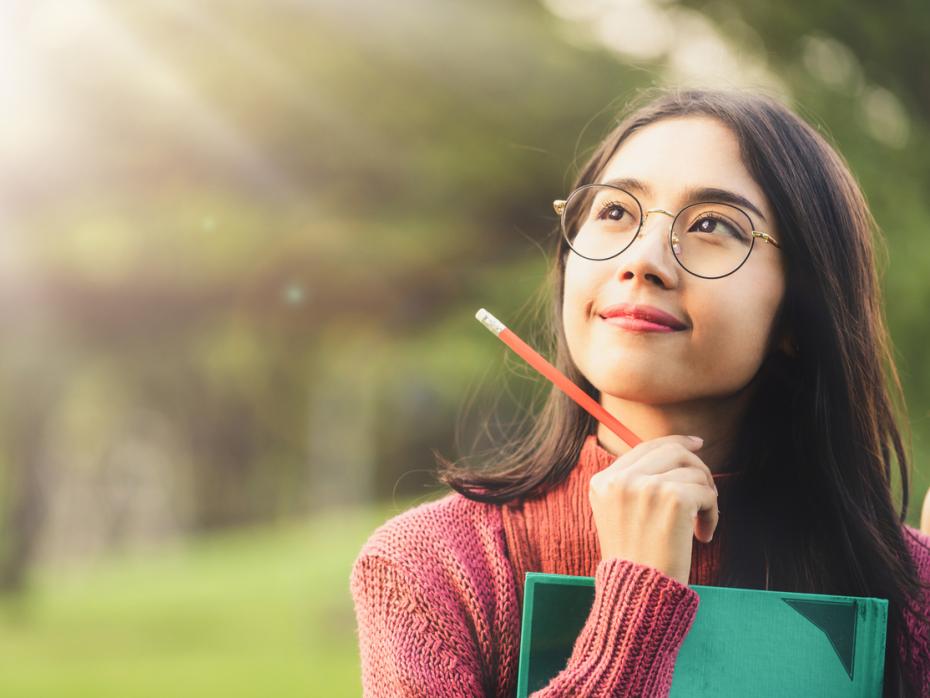 Student outside holding a notepad while thinking deeply