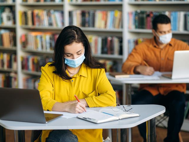 A young student wearing a mask studies in the library