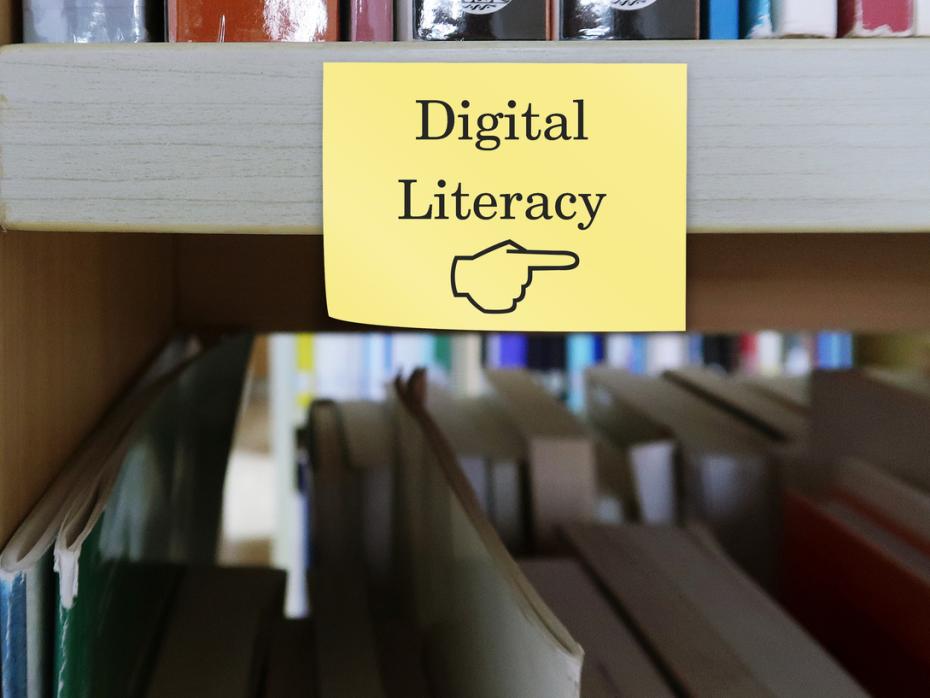 A sign saying "digital literacy" hung up on a shelf with books behind it