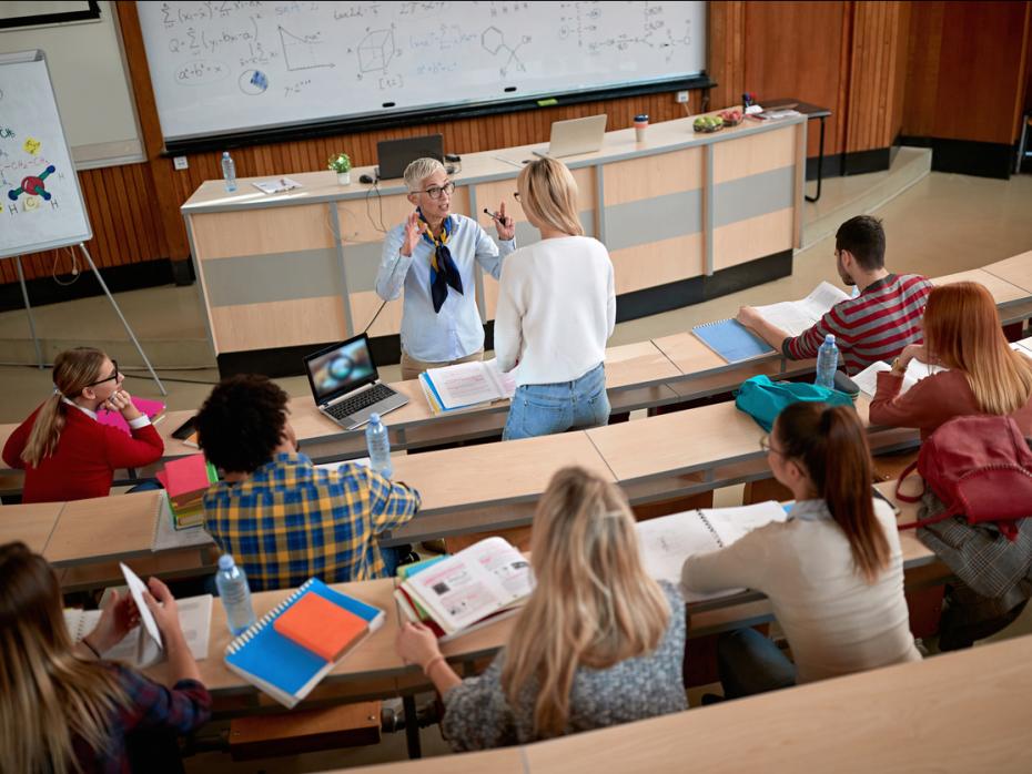 Students sitting at their desks in class while a teacher speaks