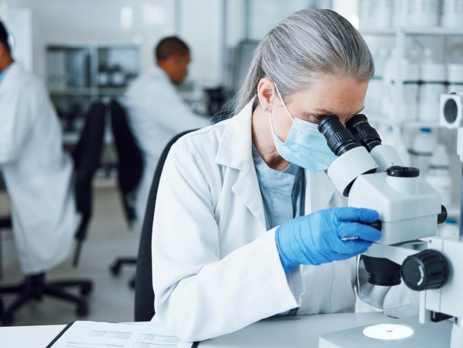 A woman in a research lab looking through a microscope