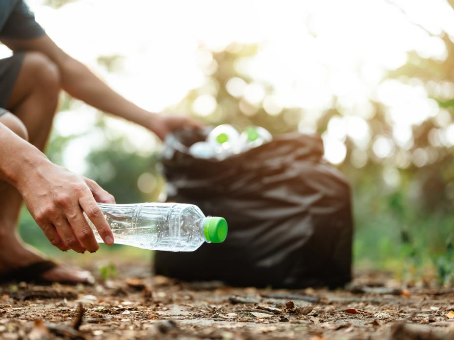 A hand picking up a plastic bottle off the ground