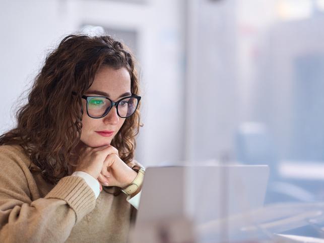 A young woman in glasses works at a laptop