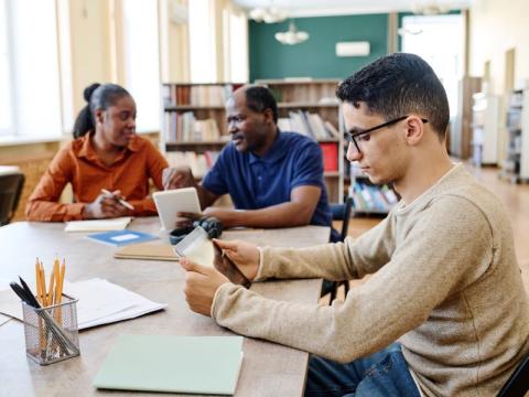 Three adult students working at a shared desk