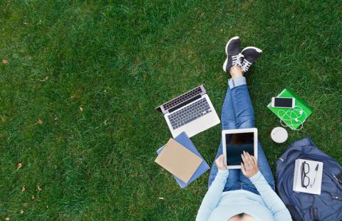 A bird's eye view shot of a woman sat on a lawn, using several devices