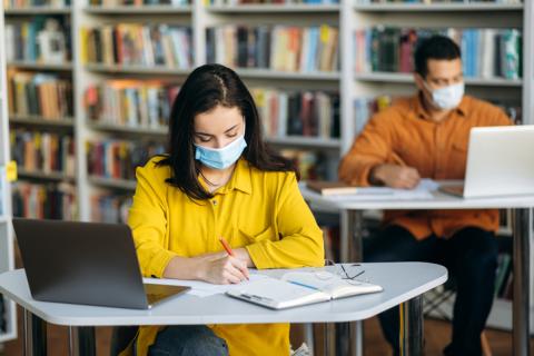 A young student wearing a mask studies in the library