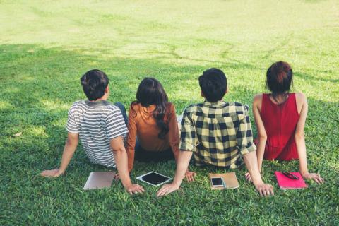 Four students sit on a grassy lawn