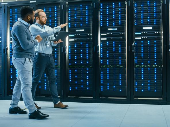 IT technician with a laptop computer and black male engineer colleague in data centre