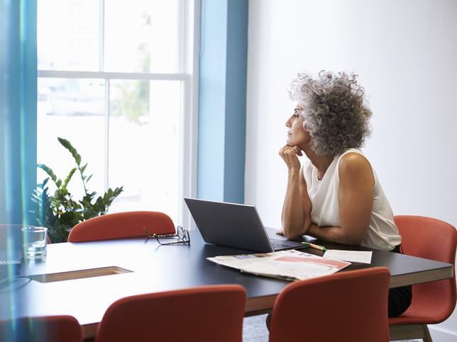 Middle-aged woman with laptop looking out office window