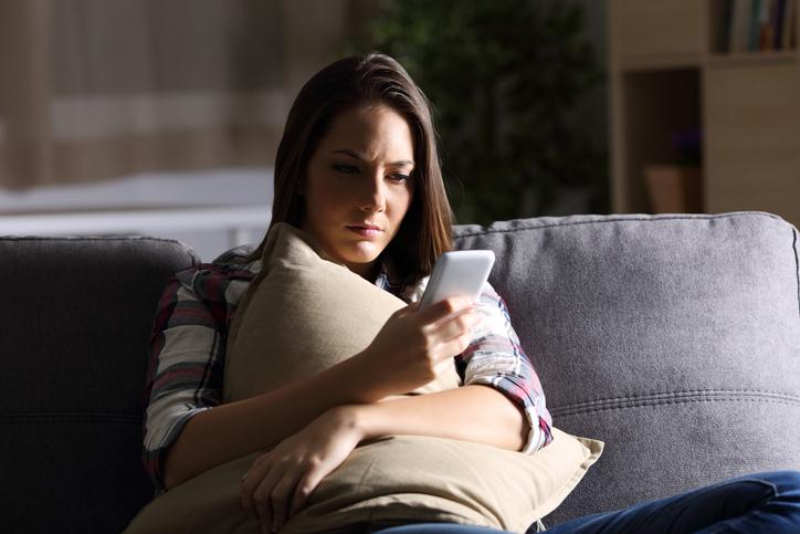 Young woman on couch with pillow looking at phone