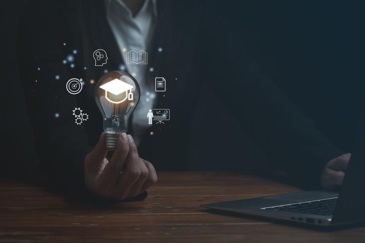 A woman holds a lightbulb with a holographic rendition of a mortarboard, 