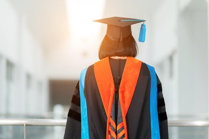 A PhD graduate in cap and gown stands with her back to the camera