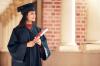 A woman in a mortarboard, holding a scroll, looks off into the distance