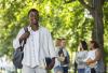 A Black student walking around campus with books in hand